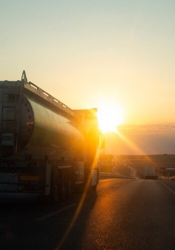 Tanker truck driving along a highway at sunset, with warm sunlight reflecting off the trailer and the road ahead.